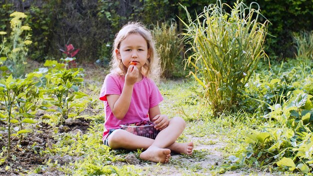 Foto portret van een meisje dat aardbeien eet terwijl het op het land zit