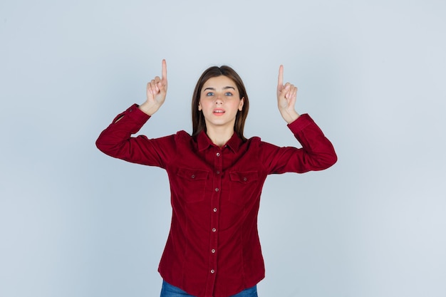 Portret van een meisje dat omhoog wijst in een bordeauxrode blouse en er zelfverzekerd uitziet