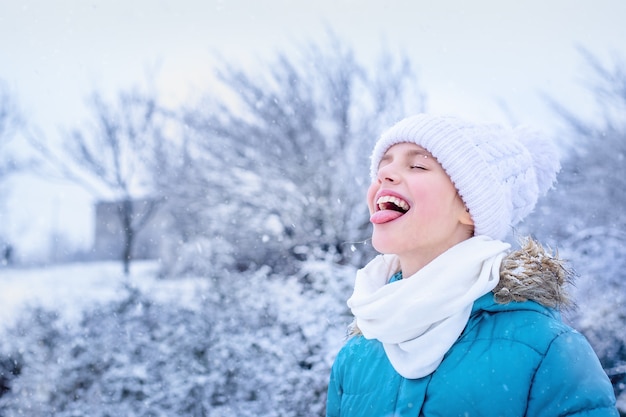 Portret van een meisje in blauwe winterkleren sneeuwvlokken vangen met haar tong in het park.