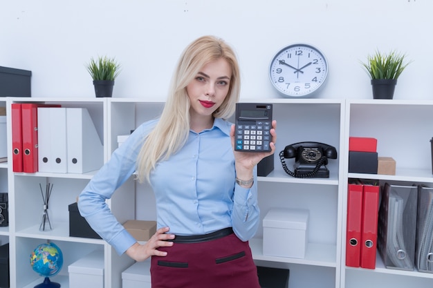 Portret van een meisje in een blauw shirt en rok rekent op een rekenmachine op kantoor