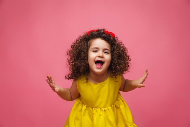 Portret van een meisje in een gele jurk schattig aantrekkelijk schattig vrolijk vrolijk klein meisje geïsoleerd roze achtergrond