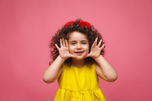 Portret van een meisje in een gele jurk schattig aantrekkelijk schattig vrolijk vrolijk klein meisje geïsoleerd roze achtergrond
