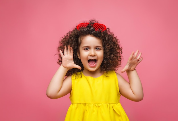 Portret van een meisje in een gele jurk schattig aantrekkelijk schattig vrolijk vrolijk klein meisje geïsoleerd roze achtergrond