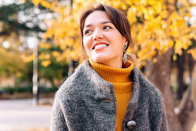 Foto portret van een meisje in een herfstpark op straat, gekleed in een grijze polto en gele jurk