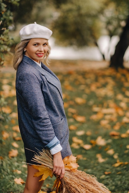 Foto portret van een meisje in een jasje en birette met een herfstboeket in een herfstpark