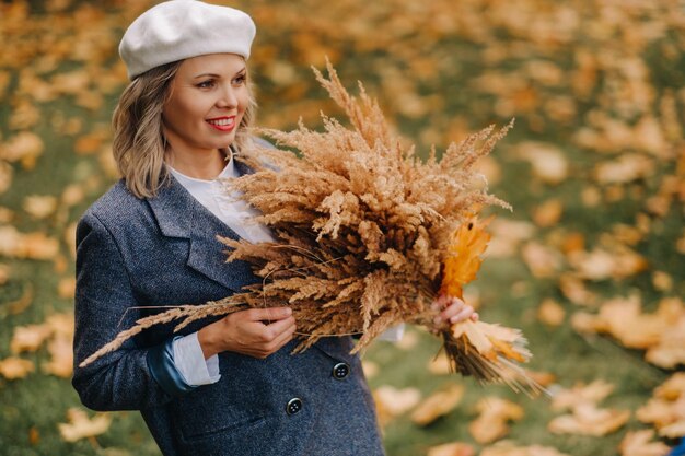 Portret van een meisje in een jasje en birette met een herfstboeket in een herfstpark