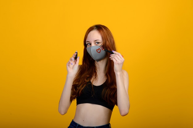 Portret van een meisje in een masker, dat een rubberen handschoen aantrekt. Gele achtergrond. Covid-19