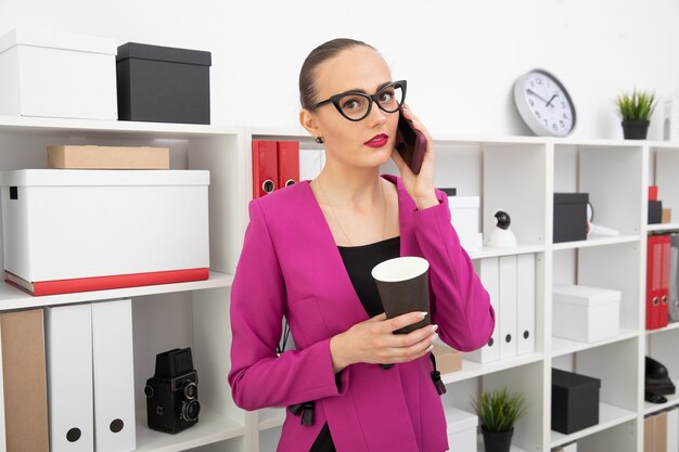 Portret van een meisje in een rok en roze jasje dat koffie drinkt en aan de telefoon praat