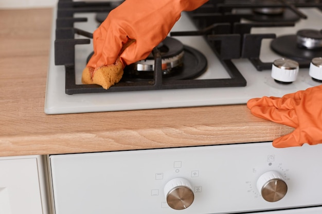 Portret van een meisje in oranje rubberen handschoenen wast een anonieme vrouw van een gasfornuis die huishoudelijke klusjes doet en de keuken schoonmaakt