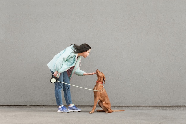 Portret van een meisje in vrijetijdskleding houdt de hond aangelijnd en speelt