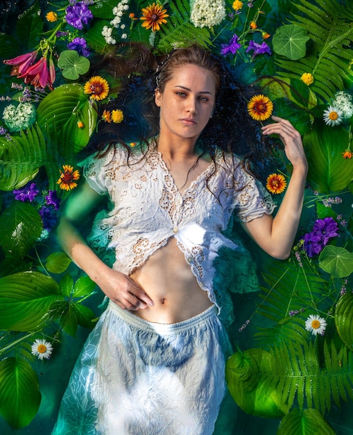 portret van een meisje in water met bloemen en groene bladeren