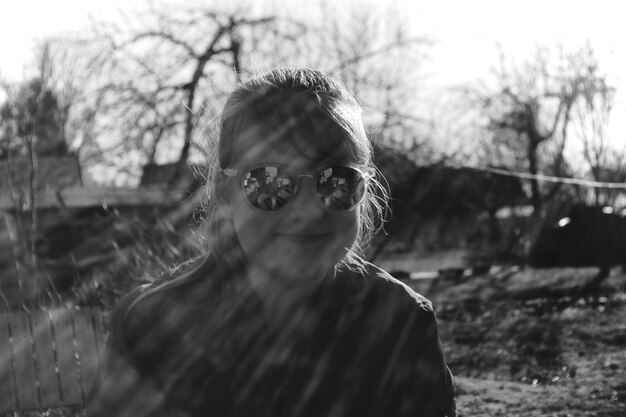 Foto portret van een meisje met een zonnebril tegen bomen op het veld