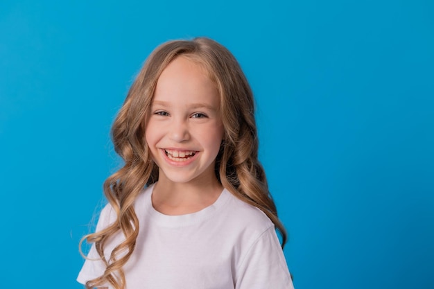 Portret van een meisje met krullend haar in jeans en een wit t-shirt op een blauwe achtergrond