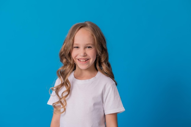 Portret van een meisje met krullend haar in spijkerbroek en een wit t-shirt op een blauwe achtergrond