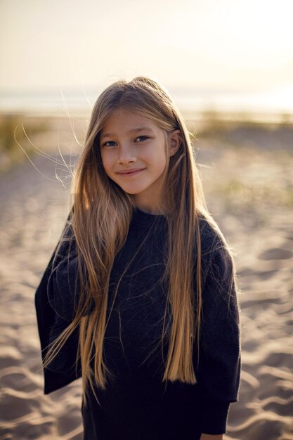 Foto portret van een meisje met lang haar dat op een zandstrand loopt in een zwart leren jasje