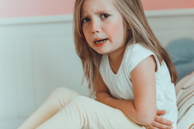 Portret van een meisje met maagpijn dat thuis op bed zit