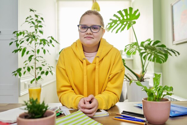 Portret van een meisje van 12 en 13 jaar oud in een geel sweatshirt met een bril die naar de camera kijkt