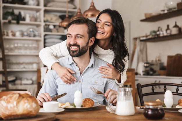 Portret van een modern Europees stel, man en vrouw die aan tafel eten terwijl ze thuis ontbijten in de keuken