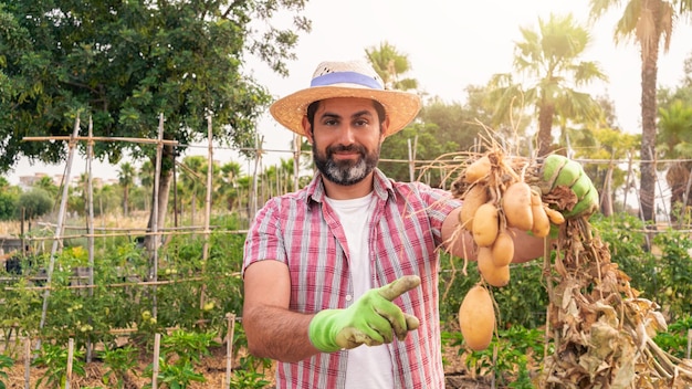 Portret van een moderne, bebaarde boer met aardappelen op handen die naar de camera kijkt