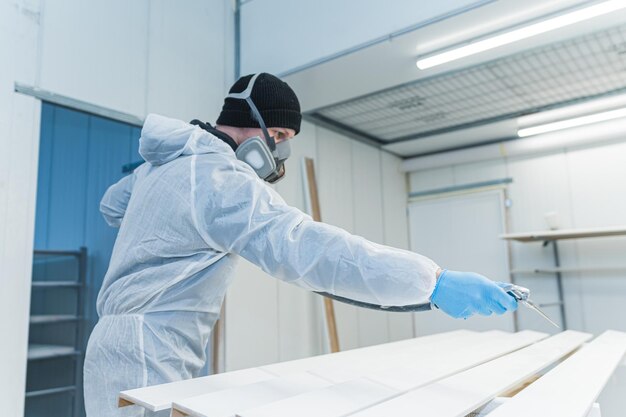 Foto portret van een moderne timmerman die een houten stuk schildert terwijl hij in een timmerwerkplaats werkt