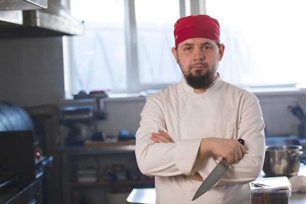 Portret van een modieuze chef-kok in bandana met een mes in een keuken, concept van koken en Haute cuisine