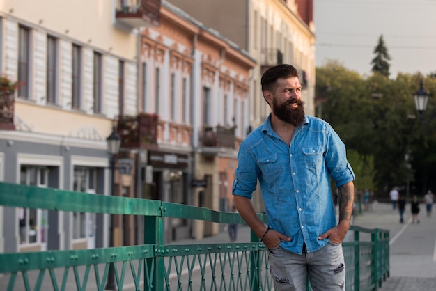 Portret van een modieuze, goed geklede man met baard die buiten poseert en wegkijkt, zelfverzekerde en gefocuste volwassen man in shirt die buiten staat op straat elegante fotomodel