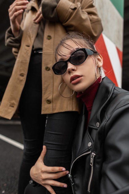 Portret van een modieuze, mooie vogue-vrouw in een stijlvolle zonnebril met een zwarte leren jas die op straat poseert