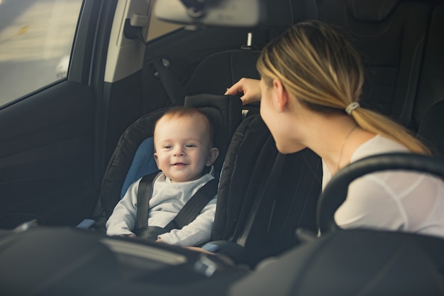 Portret van een moeder die naar een baby kijkt die op de voorstoel van de auto zit
