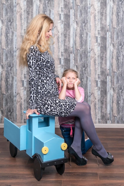 Portret van een moeder die op een houten speelgoedauto zit en een dochter die zijn handen op zijn knieën laat rusten, moeder