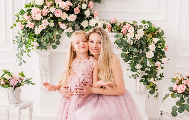 Portret van een moeder en dochter in elegante jurken in een prachtig interieur met bloemen.