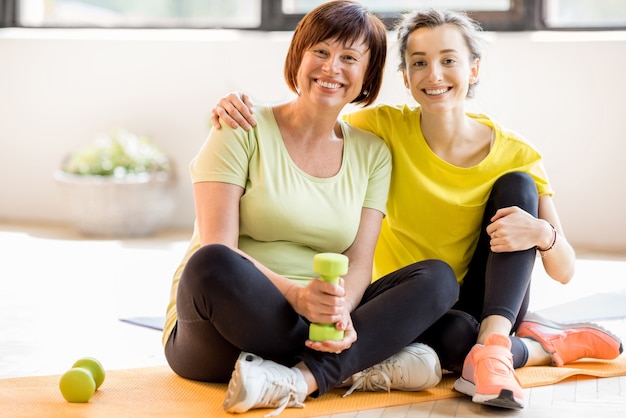 Portret van een moeder en dochter in sportkleding die samen zitten na de training binnenshuis