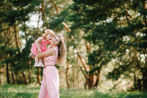 Portret van een moeder houdt dochter op handen op de natuur op zomervakantie. Moeder en meisje spelen in het park bij zonsondergang. Concept van vriendelijke familie. Detailopname.