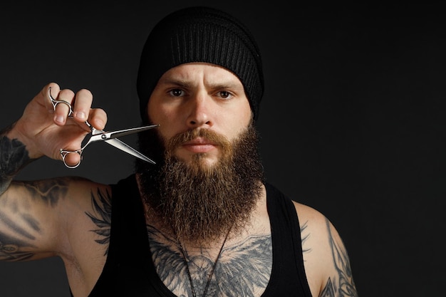 Portret van een moedige man met een baard, hij houdt een schaar bij zijn baard en kijkt naar de camera.