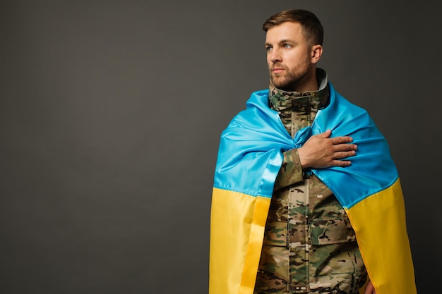 Portret van een moedige Oekraïense militaire man vastgebonden met de vlag van Oekraïne en hand in hand op het concept van hartvrijheid