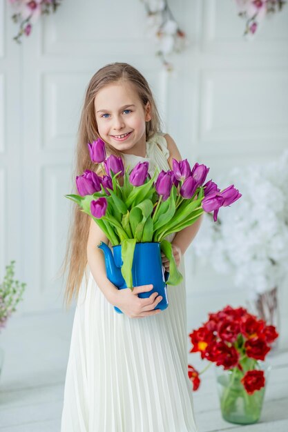 Portret van een mooi blauwogig kind een klein meisje met een boeket tulpen in een lichte kamer