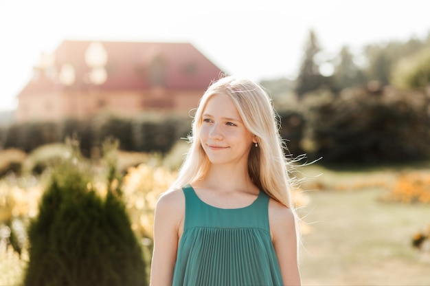 Portret van een mooi charmant aantrekkelijk blond meisje in een groene jurk buiten in een zomers zonnig park glimlachend happy positive lady op natuurlijke achtergrond