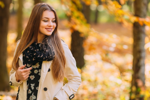 Portret van een mooi, dromerig en glimlach meisje met lang haar in mooie witte jas en sjaal staande in een park in de herfst.