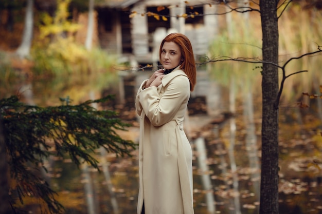 Portret van een mooi, dromerig en verdrietig meisje met rood haar in de herfst van de witte vacht