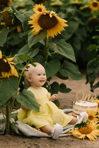 Portret van een mooi, gelukkig eenjarig meisje met een taart in een veld met zonnebloemen