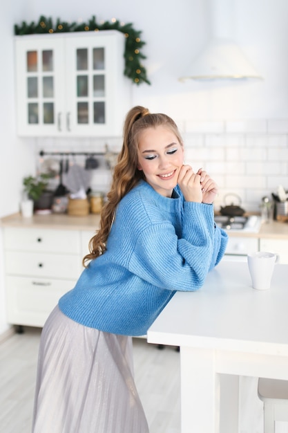 Portret van een mooi gelukkig schattig meisje met een kapsel in een blauwe trui in een ingerichte keuken