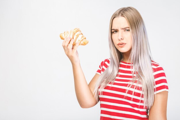 Portret van een mooi jong blond geschikt meisje dat een rode bovenkant draagt die een croissant houdt