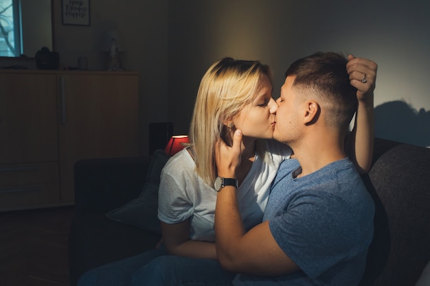 Portret van een mooi jong Kaukasisch paar dat 's nachts op de bank thuis zit te kussen terwijl de man het gezicht van haar vriendinnen aanraakt.