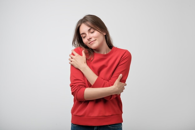 Portret van een mooi jong meisje in een rood shirt dat zichzelf knuffelt