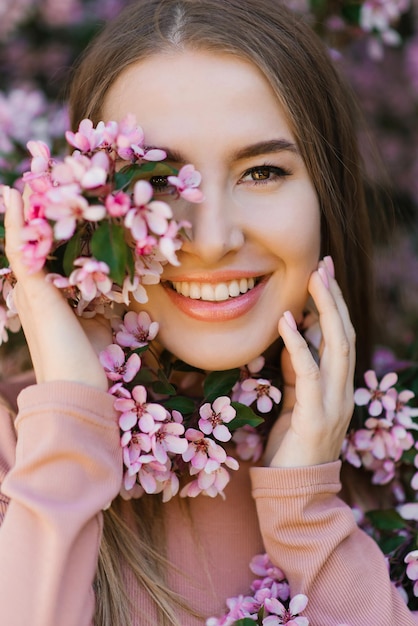 Portret van een mooi jong meisje in het voorjaar in de buurt van een bloeiende roze appelboom
