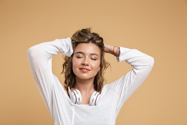 Portret van een mooi jong meisje met een jurk die geïsoleerd over een gele muur staat en naar muziek luistert met een koptelefoon