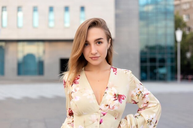 Portret van een mooi jong meisje op een achtergrond van een blauw zakencentrum gekleed in een zomerse beige jurk