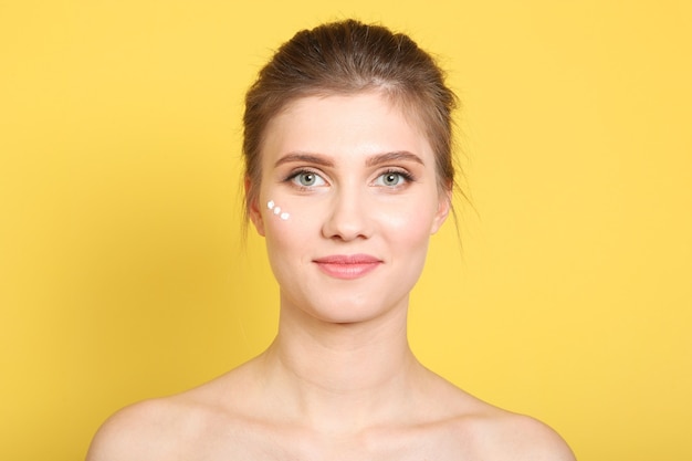 Portret van een mooi jong meisje op een gekleurde achtergrond die verzorgende crème gebruikt