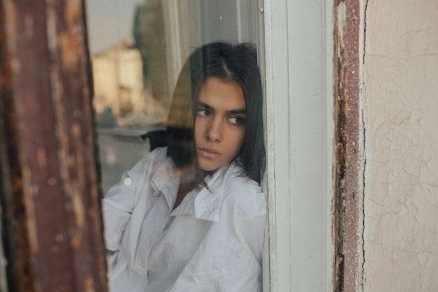 Portret van een mooi jong verdrietig meisje kijkt uit het raam.