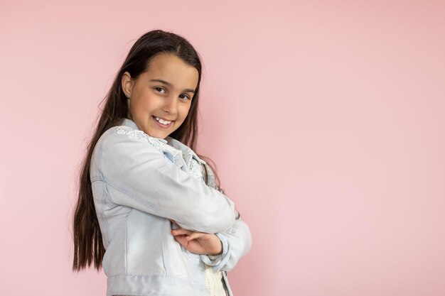 Portret van een mooi kind dat op zoek is en een broek draagt die over een roze achtergrond is geïsoleerd.