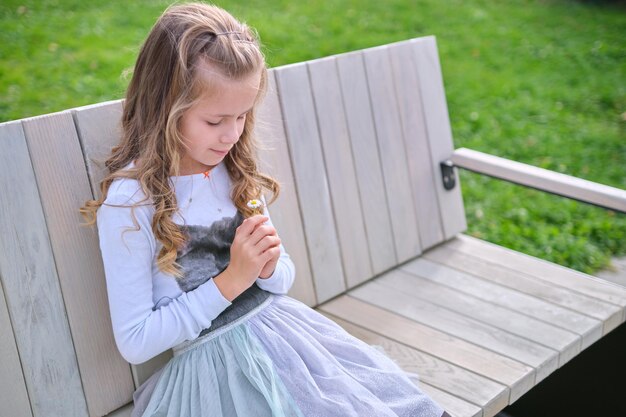 Portret van een mooi kindmeisje dat buiten op een bankje zit